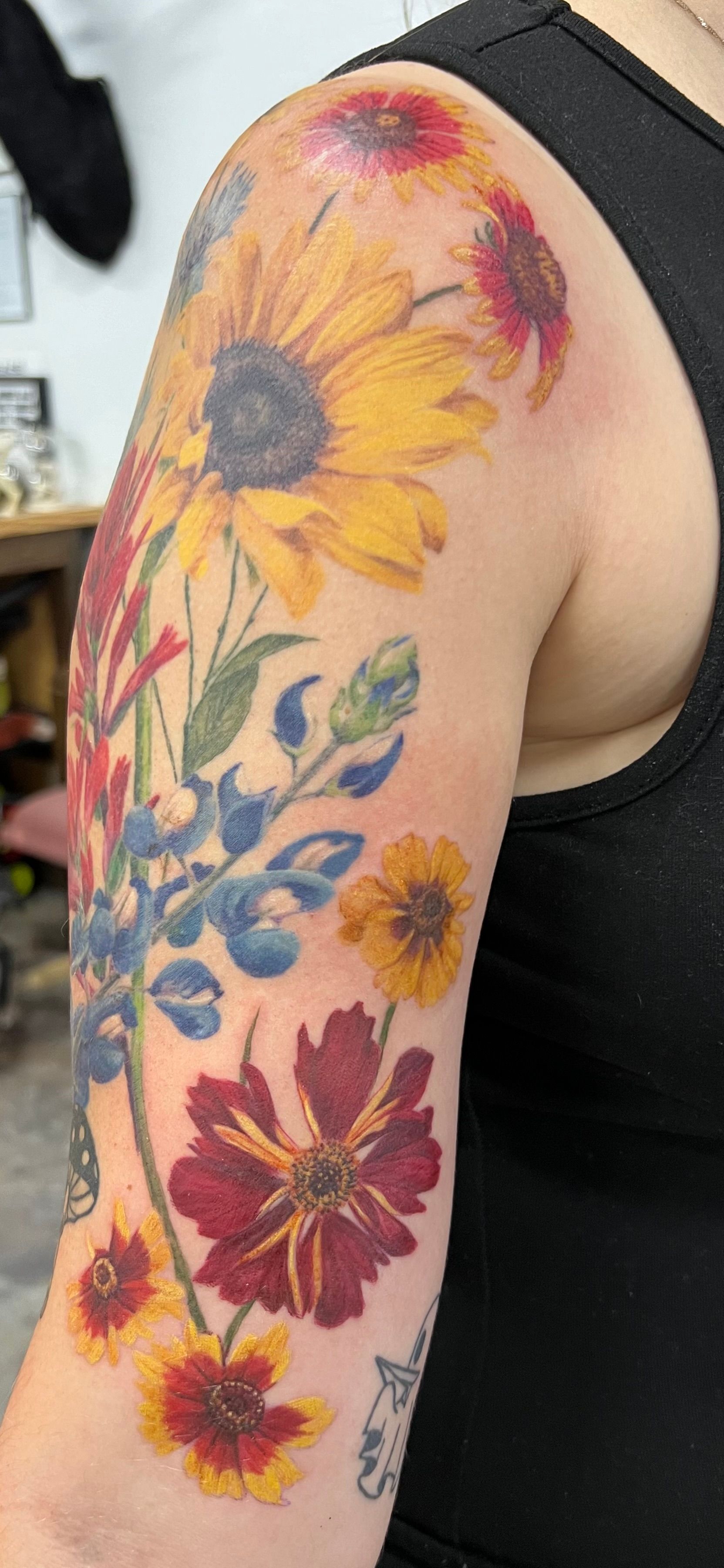 Tattoo of colorful flowers on a person's arm, including sunflowers, red, and blue flowers.