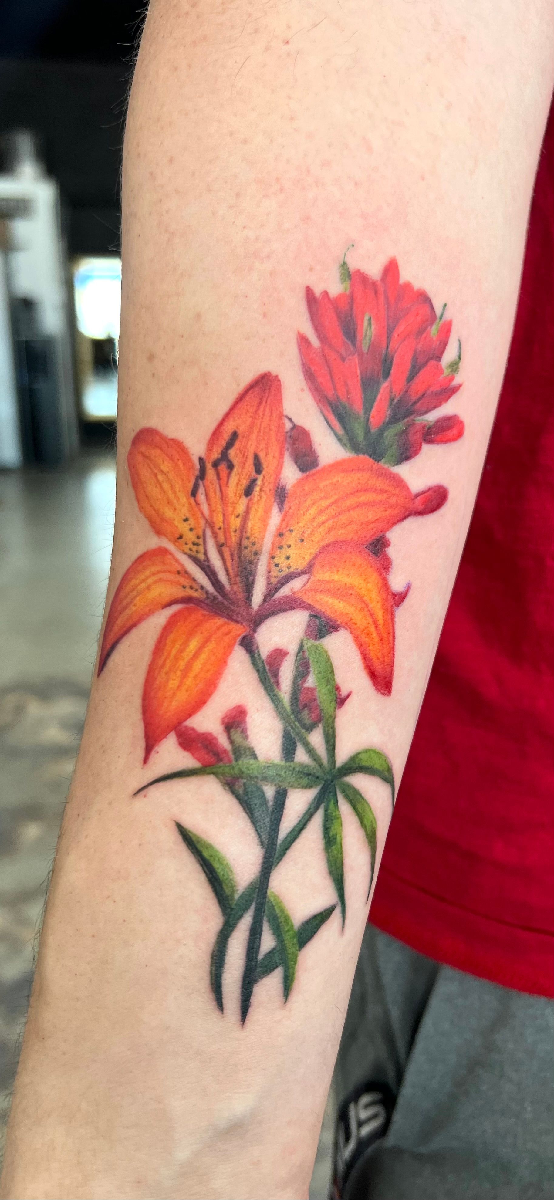 Tattoo of orange flowers on a person's arm. Includes a tiger lily and Indian paintbrush.