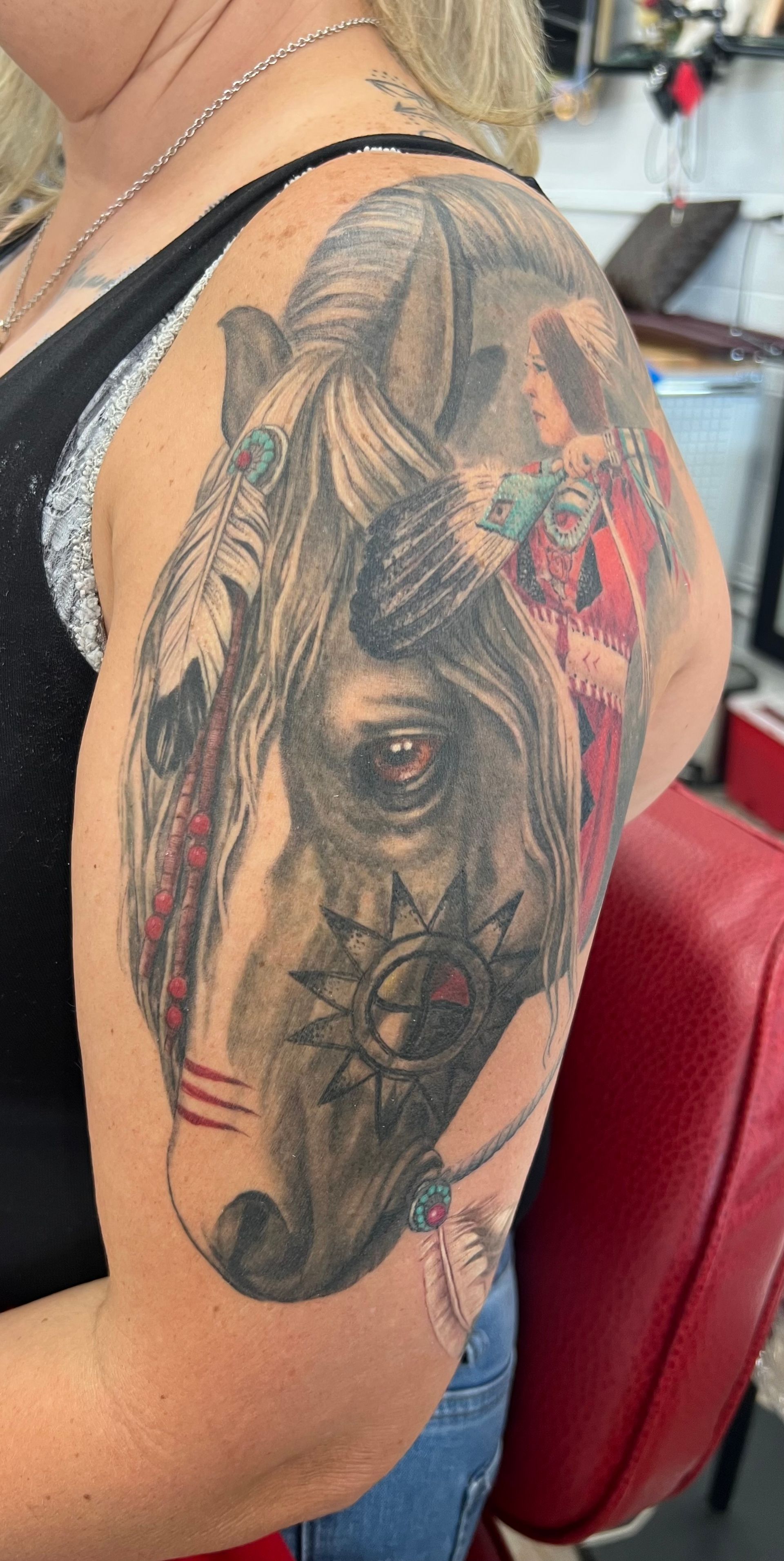 Tattoo of a horse head with Native American elements on a woman's arm.