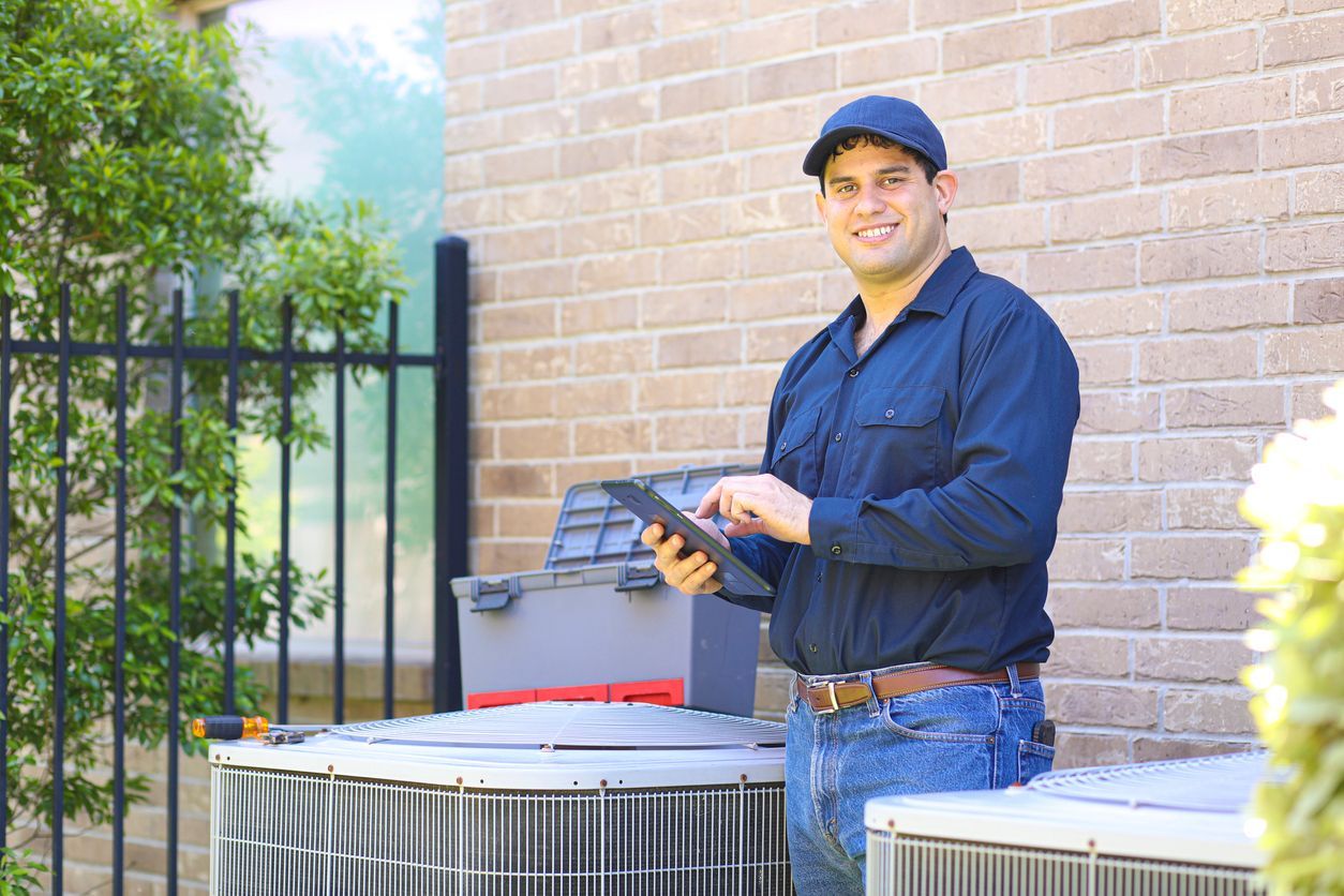 a man is standing in front of a brick building holding a tablet inspecting an AC unit.