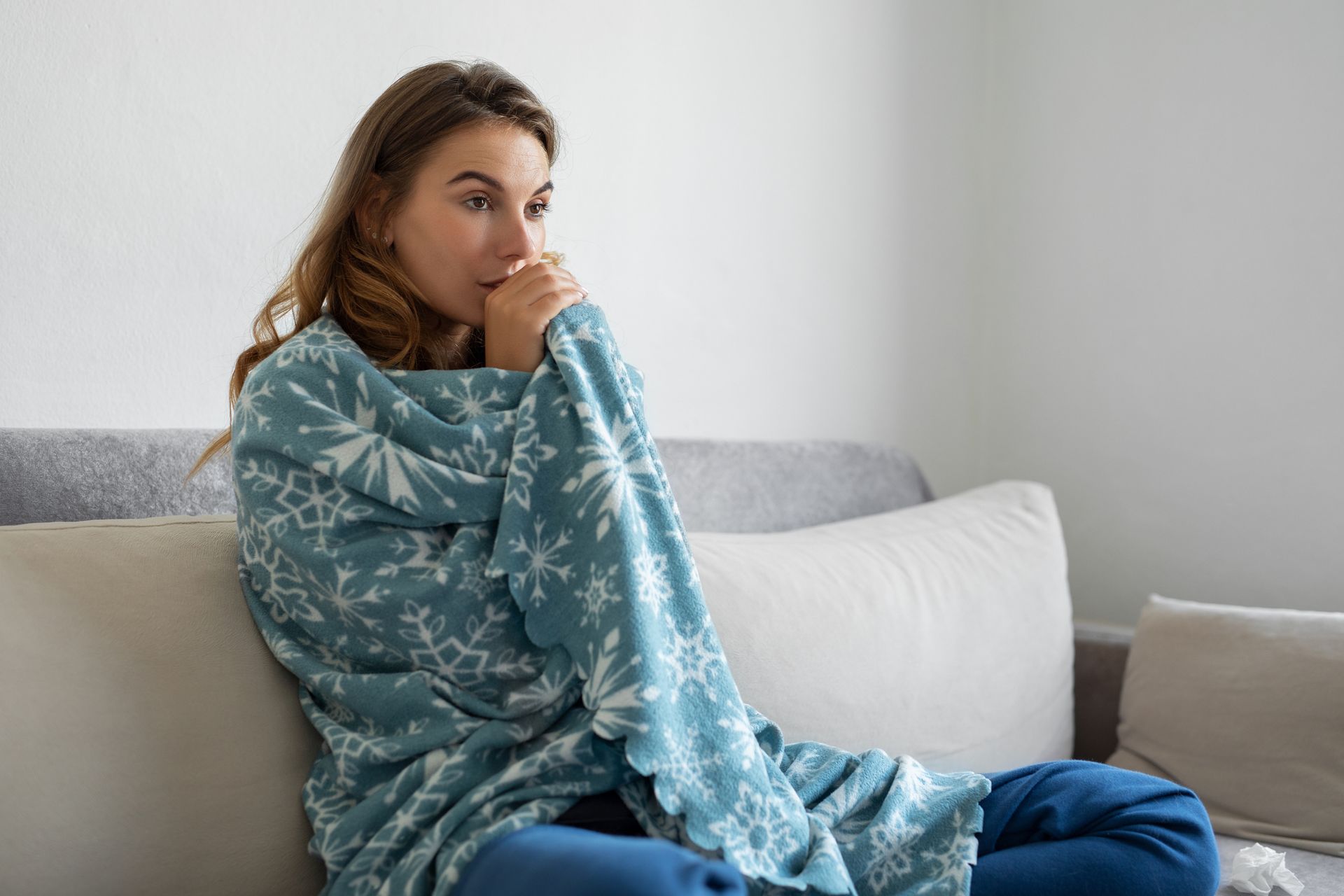 A woman warming up under a blanket in Spring, TX. Showing a need for furnace repairs.