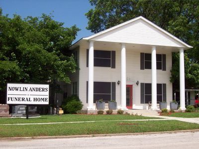 Nowlin Anders Funeral Home sign beside a white two-story building with columns and a red roof