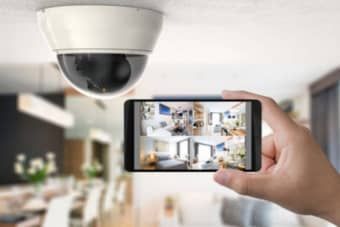 A person is holding a cell phone in front of a white security camera attached to the ceiling.