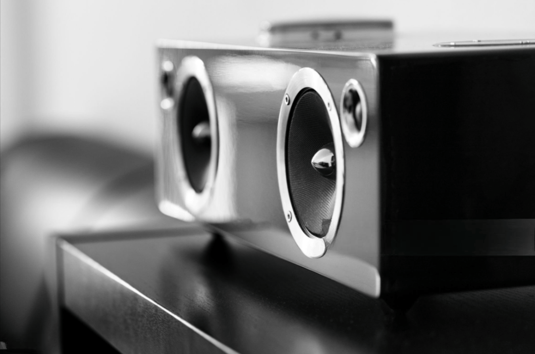 Black and white photo of a modern wireless stereo speaker with two large circular speakers and a smaller one.