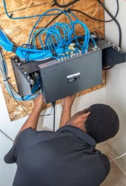 A man is installing a network hub with cables mounted to the wall in a room.