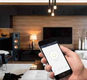 A person is holding a smartphone in their hand inside a living room to control the audio and video.