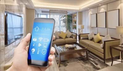 A person is holding a smartphone in the living room of an automated home.