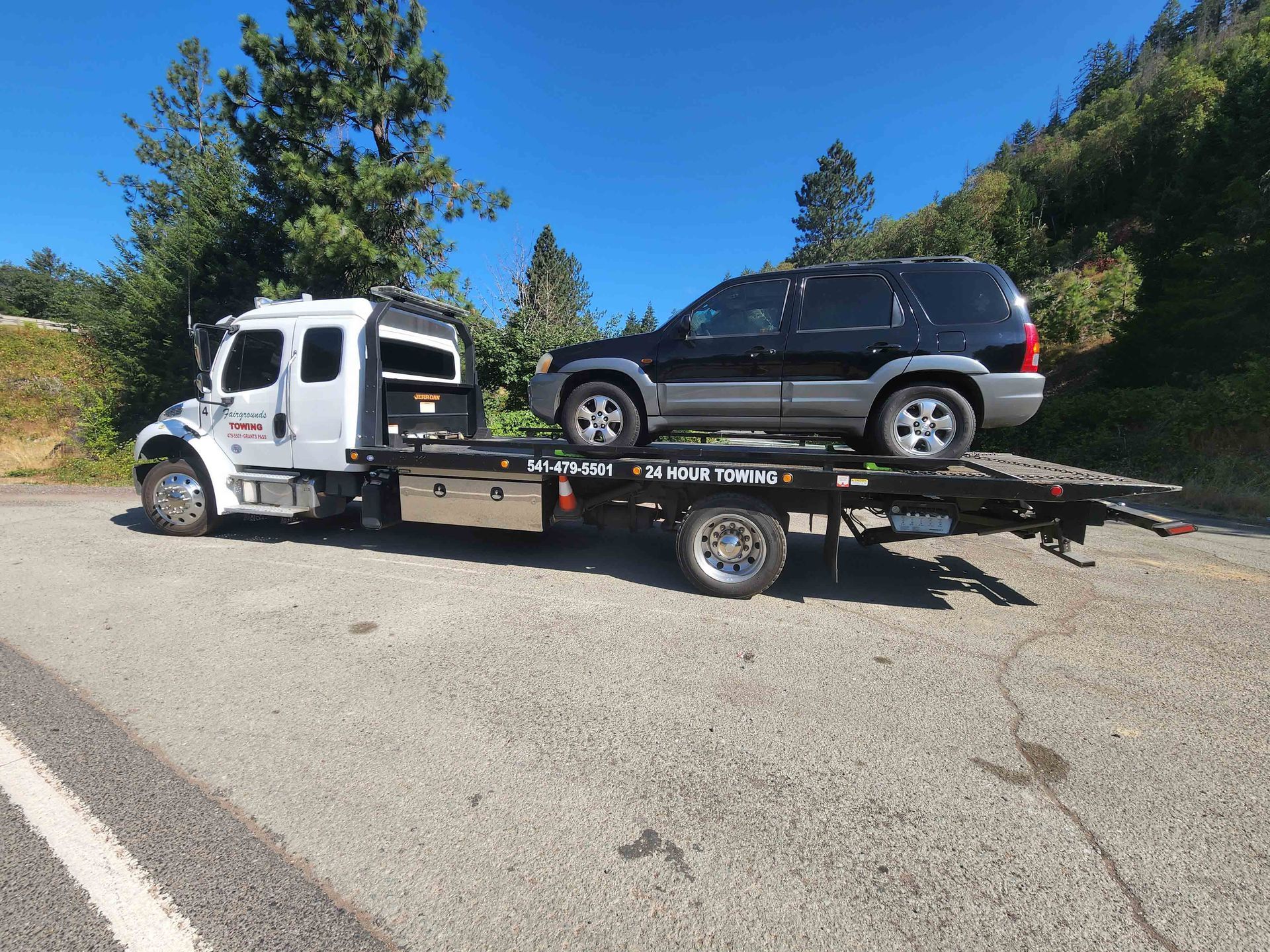 A Tow Truck Is Towing A Black SUV — Grants Pass, OR — Fairgrounds Towing & Fuel LLC