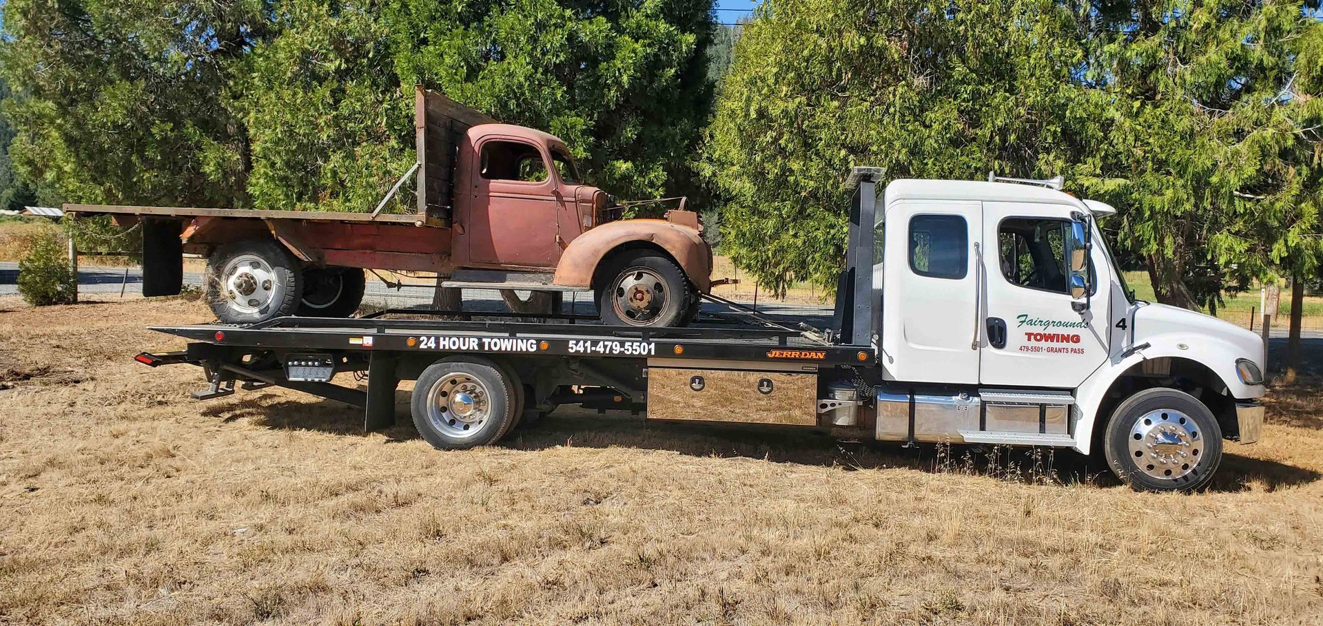 A Tow Truck Is Carrying A Rusty Truck On The Back Of It — Grants Pass, OR — Fairgrounds Towing & Fuel LLC