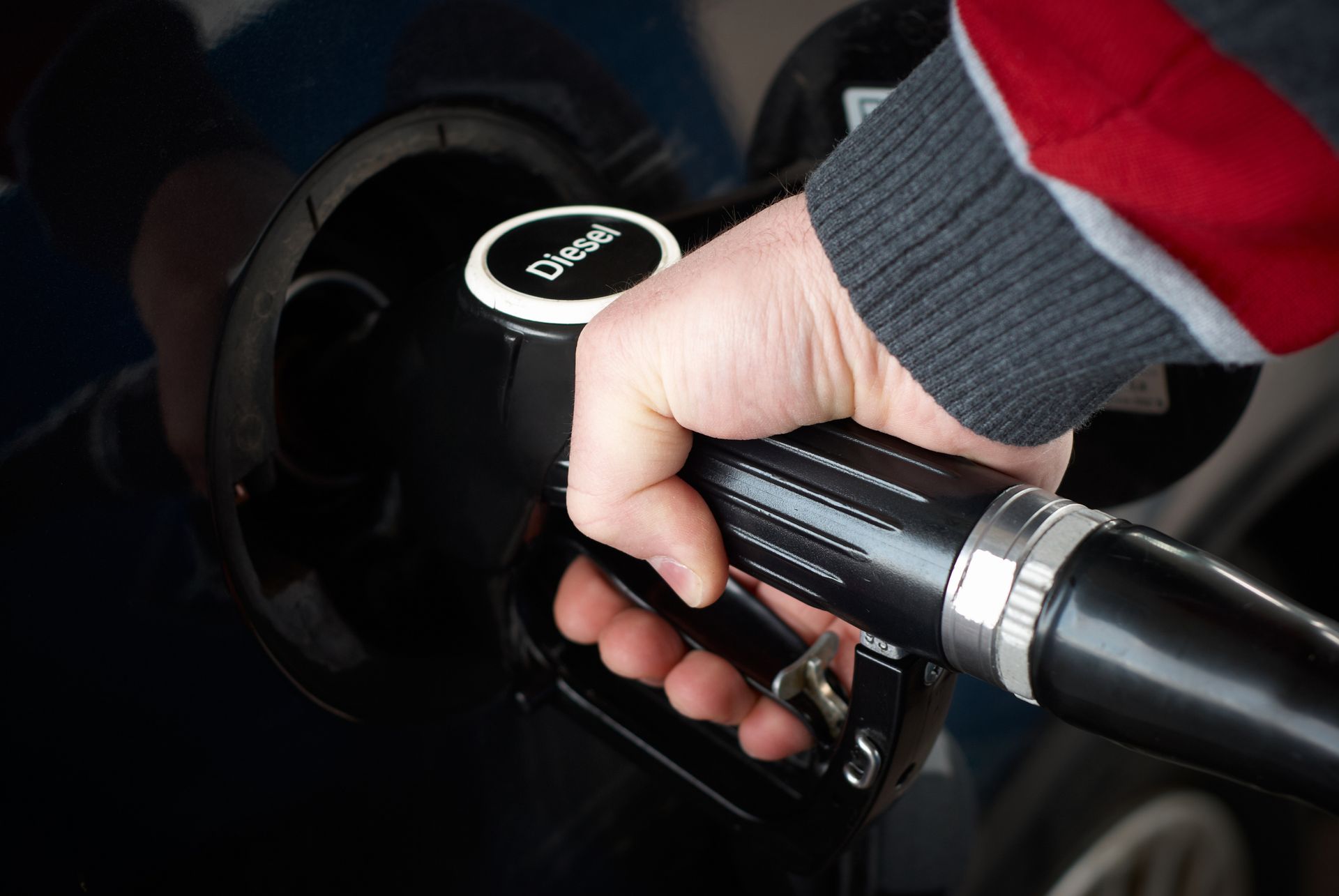 Hand holding a diesel fuel nozzle while refueling a vehicle at a gas station.