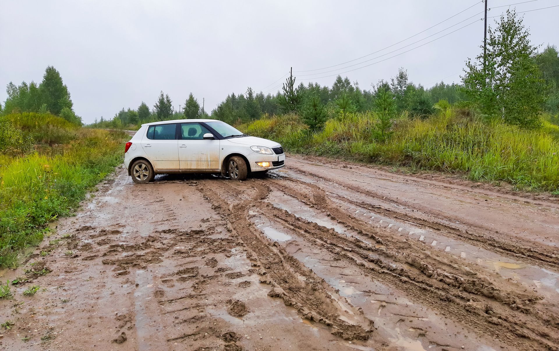 A white passenger hatchback stuck on a muddy road in rainy weather. A white passenger hatchback stuck on a muddy road in rainy weather.