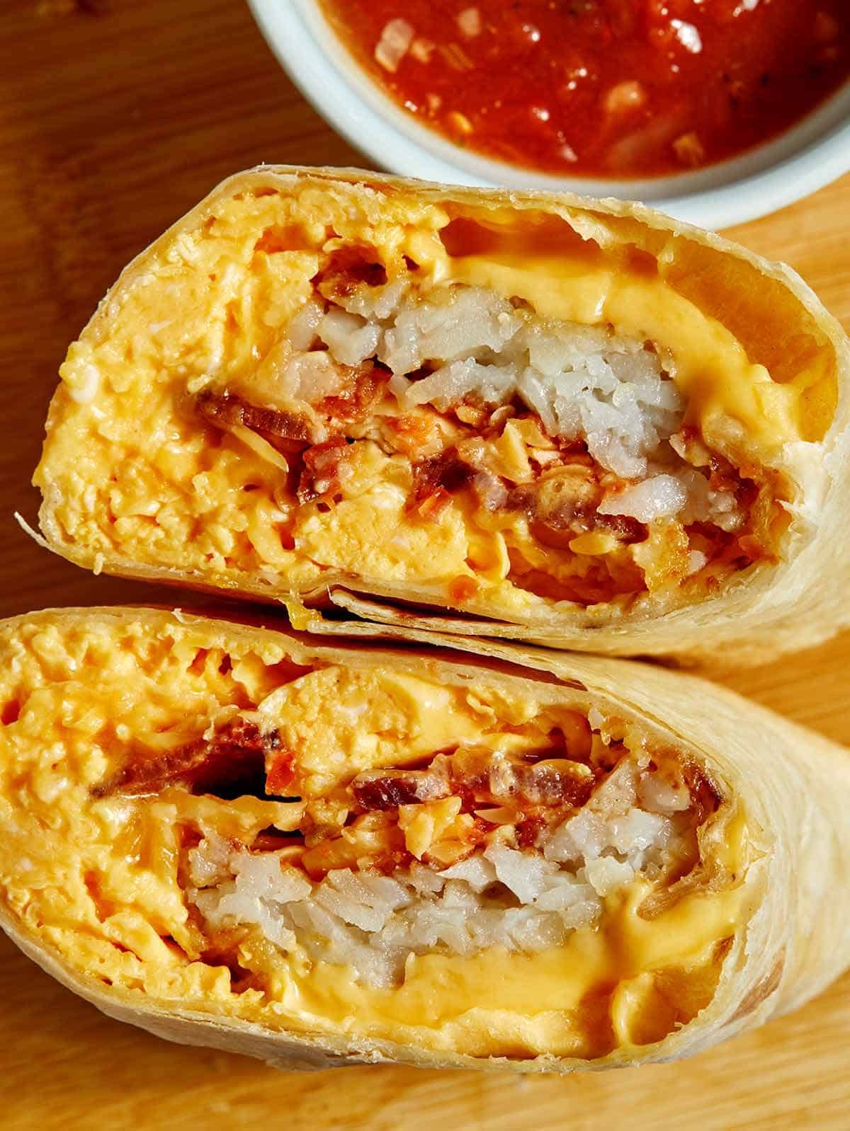 Burrito cut in half, filled with cheese, rice, and meat, with a small bowl of sauce.