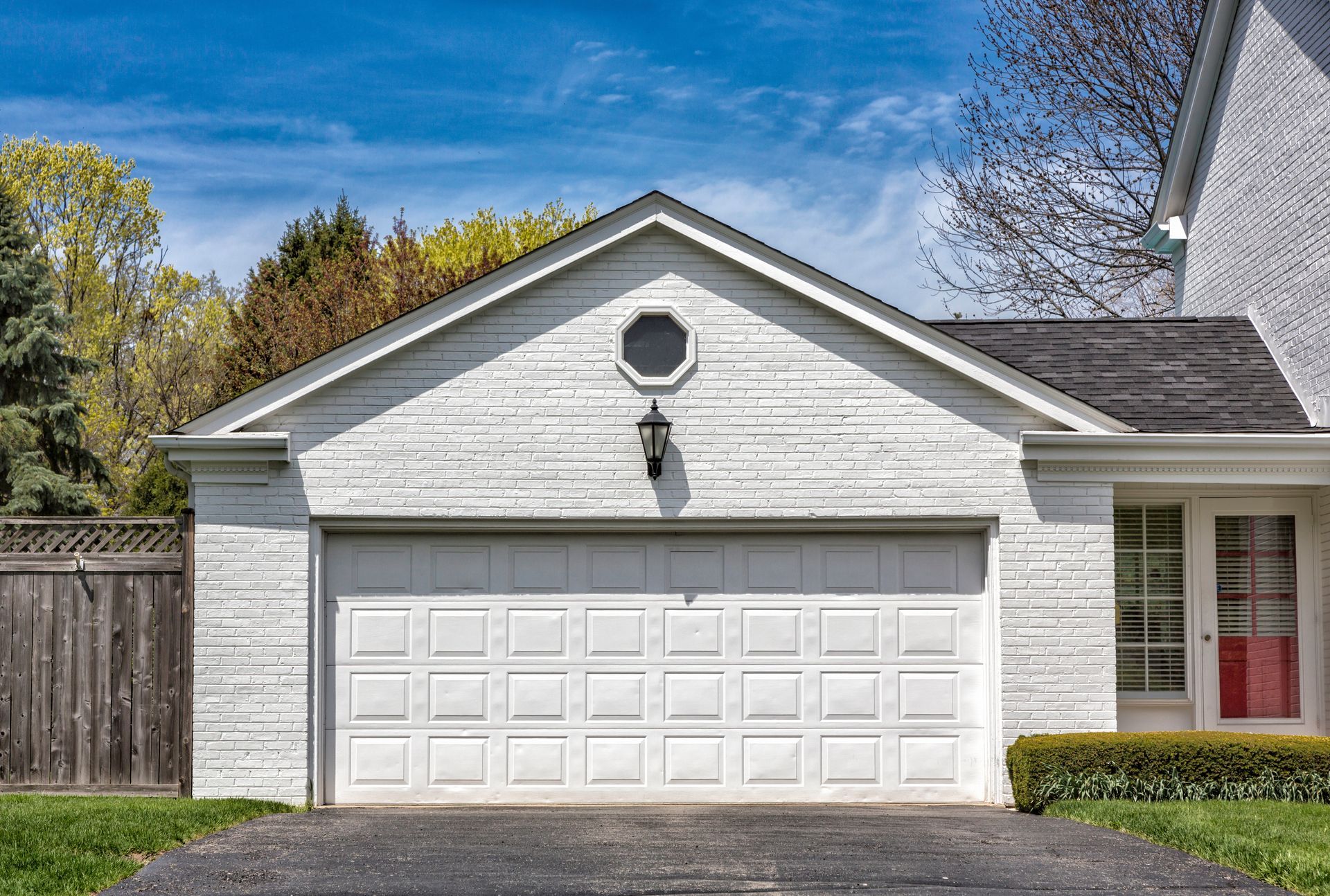 White garage with a closed door, surrounded by greenery and a blue sky.