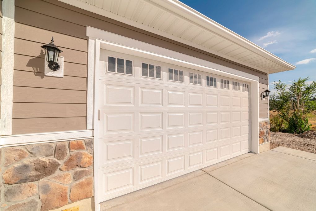 White garage door with windows, brown siding, stone accents, and a concrete driveway.