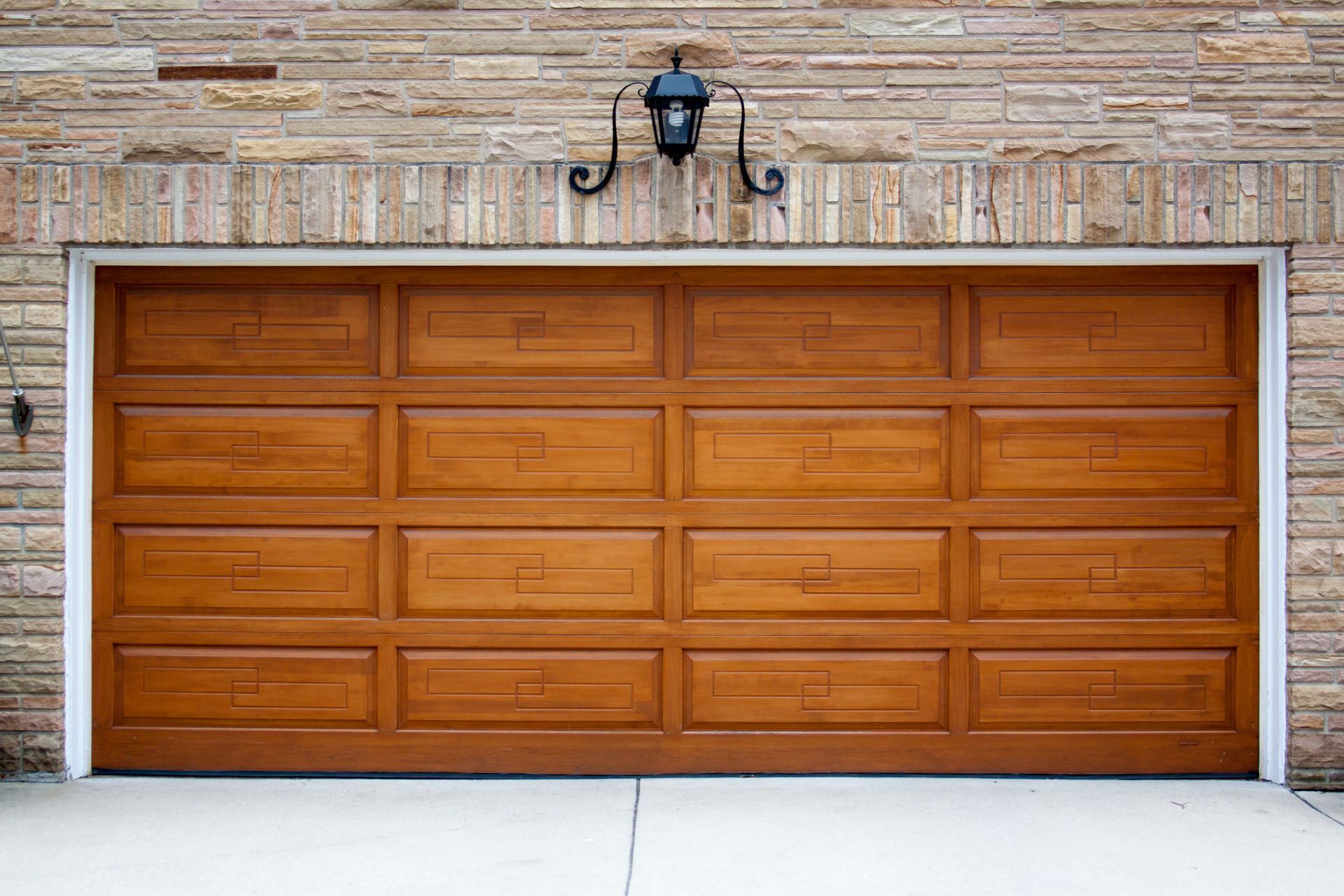 Wooden garage door, brown with panel details, beneath brick wall, with light fixture above.