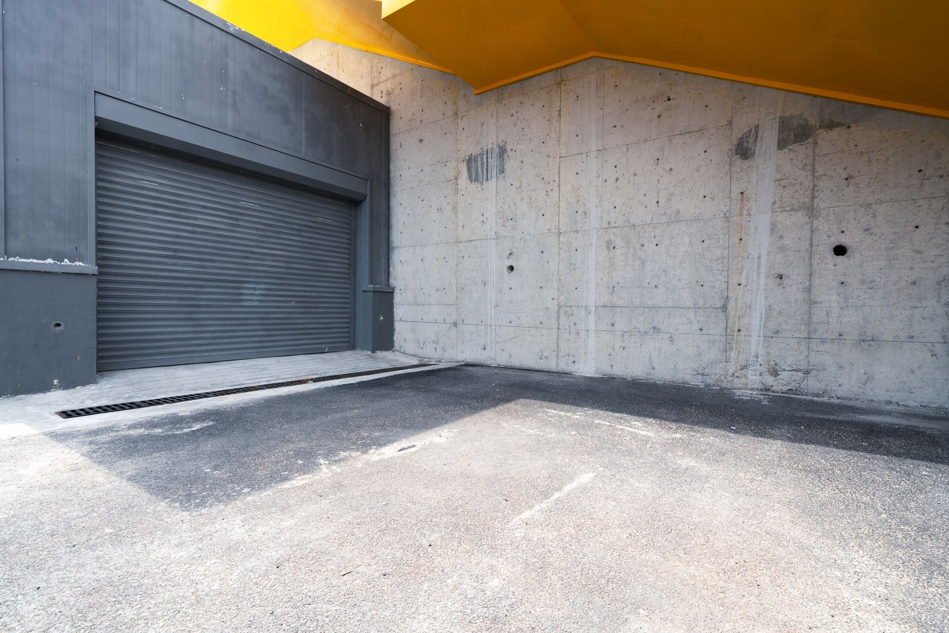 Gray roll-up door in a concrete alcove, with a yellow overhang and asphalt floor.