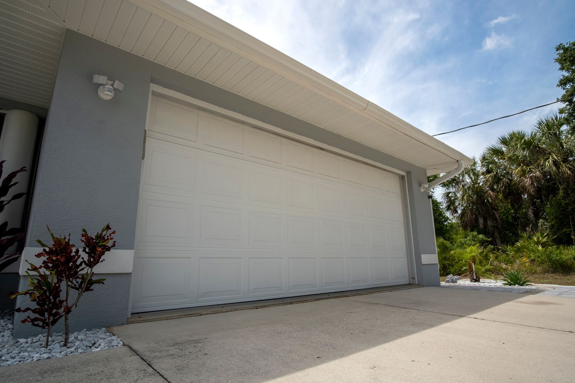 White garage door on a gray stucco house; bright sunlight and blue sky.