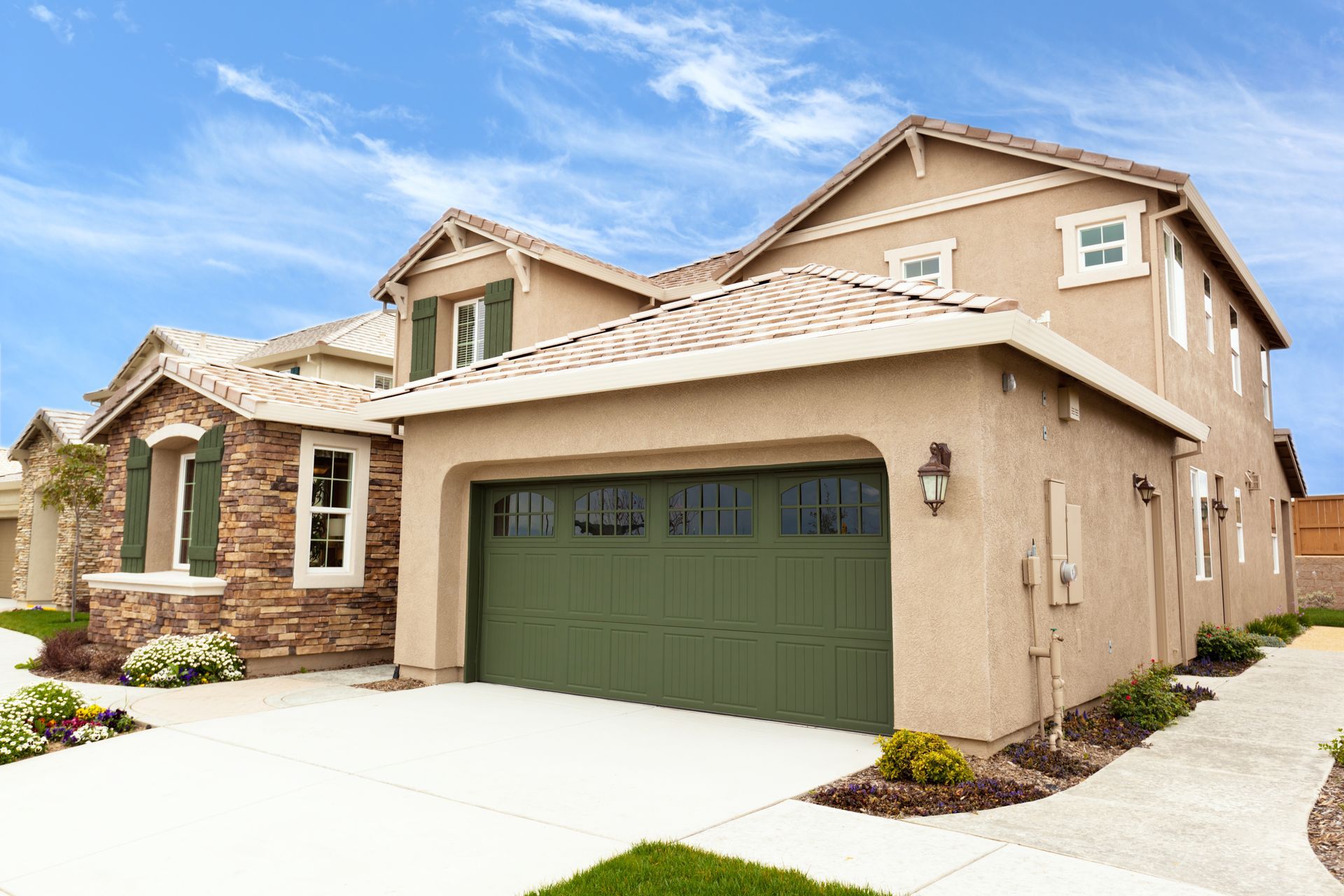 Tan two-story house with green garage door, driveway, and blue sky.