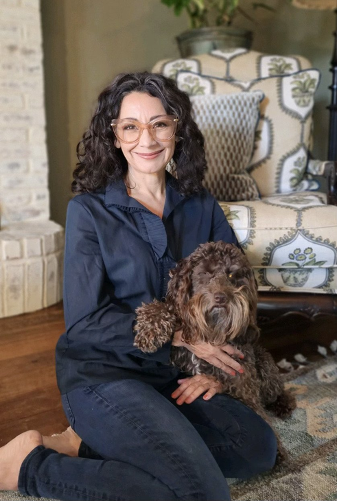 A woman is kneeling down on the floor holding a dog.