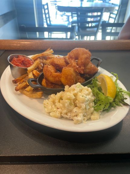 Hand holding a white bowl of pasta with orange sauce and three meatballs, against a green leaf background.