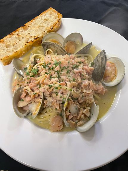 Seafood pasta with clams and a slice of bread on a white plate