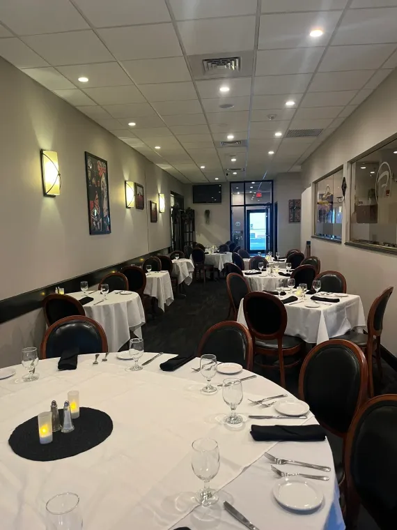 Restaurant dining room with white tablecloths, black chairs, and artwork on the walls.