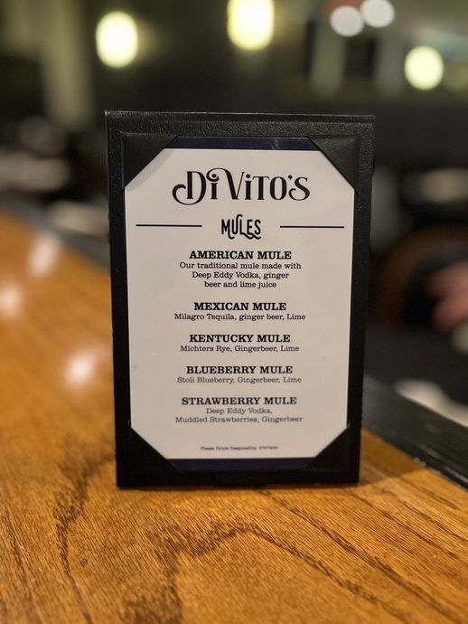 People at a bar, some drinking, conversing. Indoor setting, bar with lights, patrons.