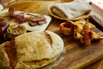 Bread, meats, and preserves on a wooden board, ready for serving.