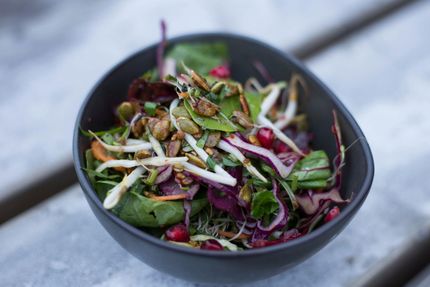 Salad with sprouts, pomegranate seeds, and toasted seeds in a dark bowl.