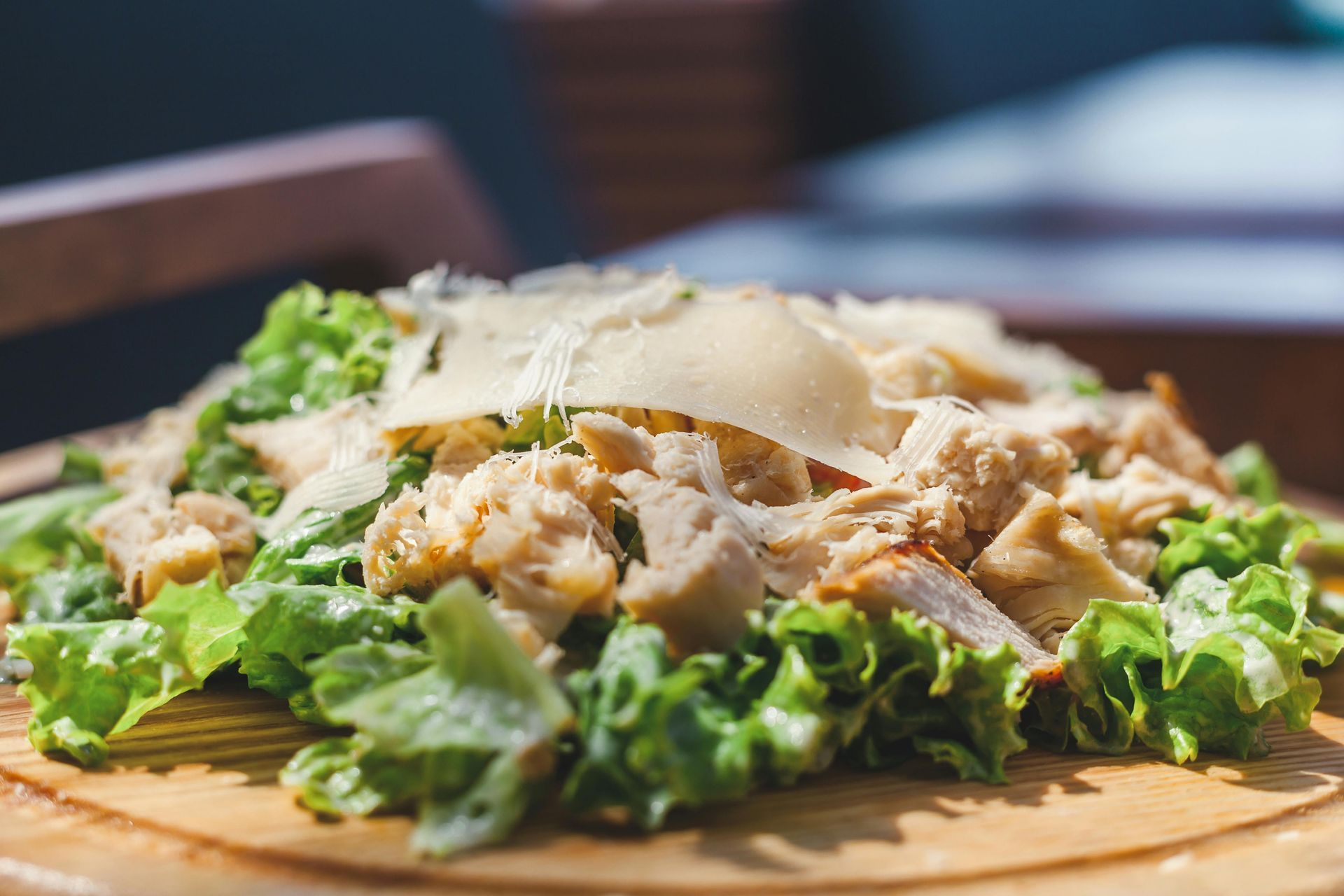 Chicken Caesar salad on a wooden board with lettuce, chicken, and parmesan cheese.