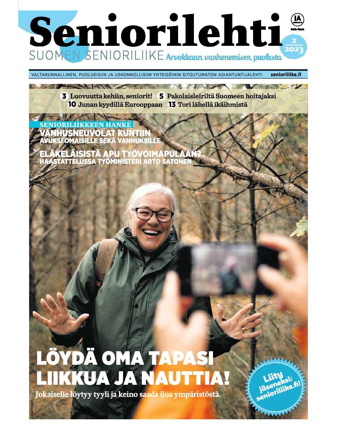 Mies hymyilee metsässä ja ojentaa kädet kuvattaessa. Lehden kansi: 