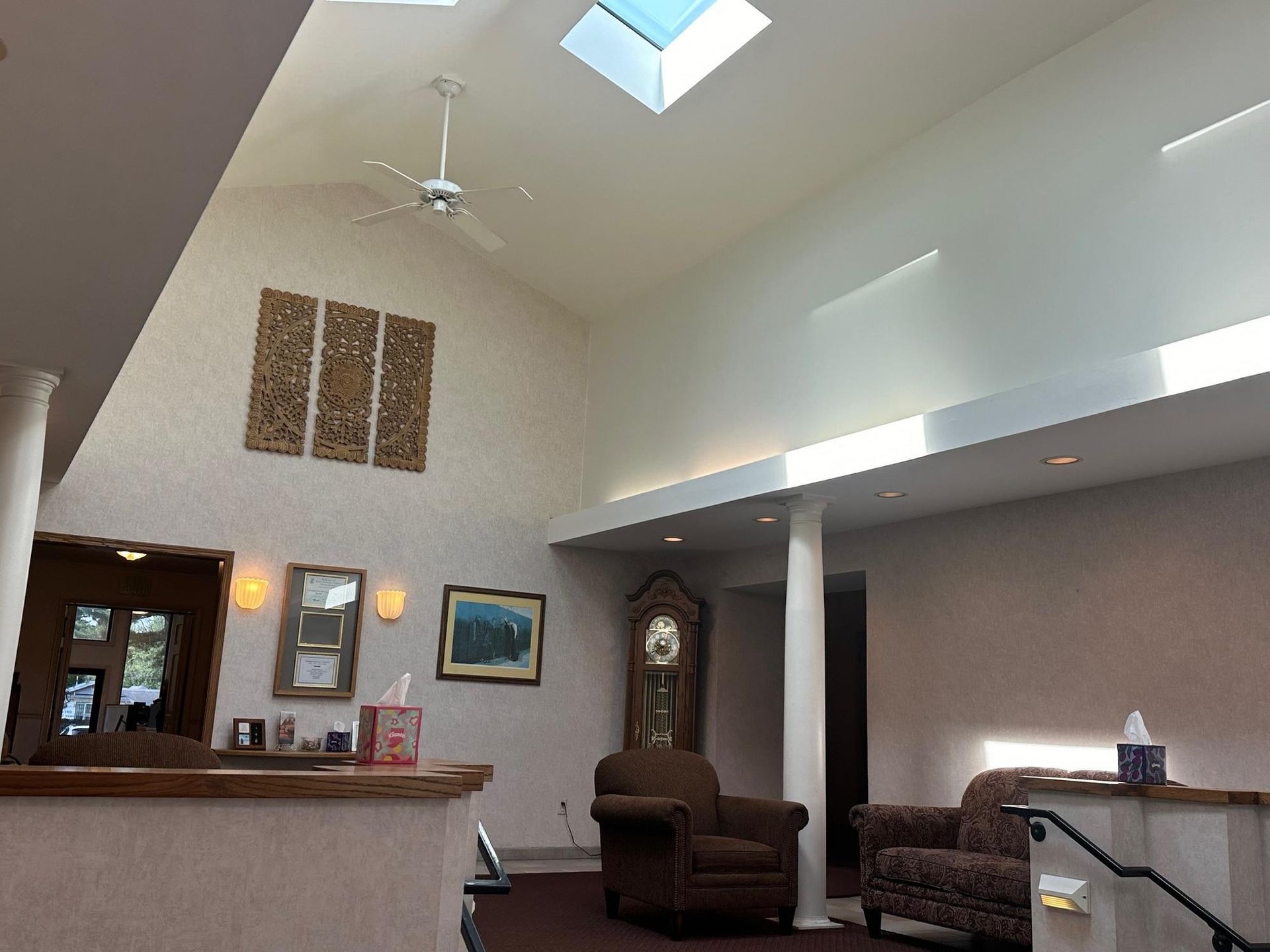 Lobby with vaulted ceiling, skylight, art, chairs, and grandfather clock. Light streams in.