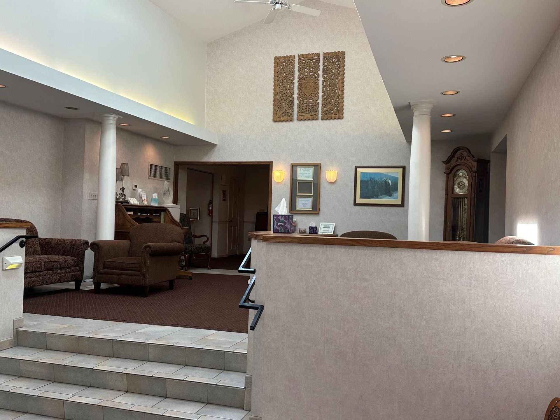 Reception area with stairs, brown carpet, seating, and a grandfather clock.