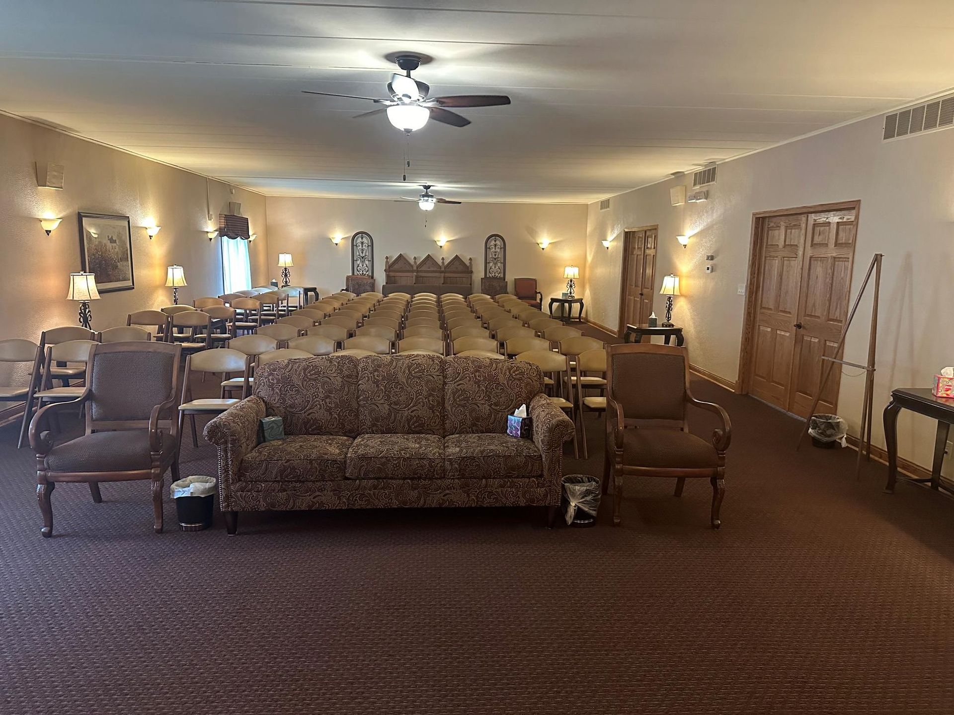 Interior of a chapel with rows of chairs, a sofa, and ornate doors.