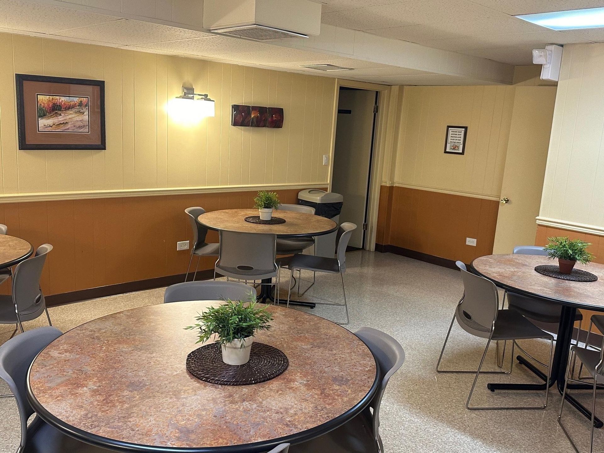 Dining area with round tables, chairs, plants, artwork, and beige and orange walls.