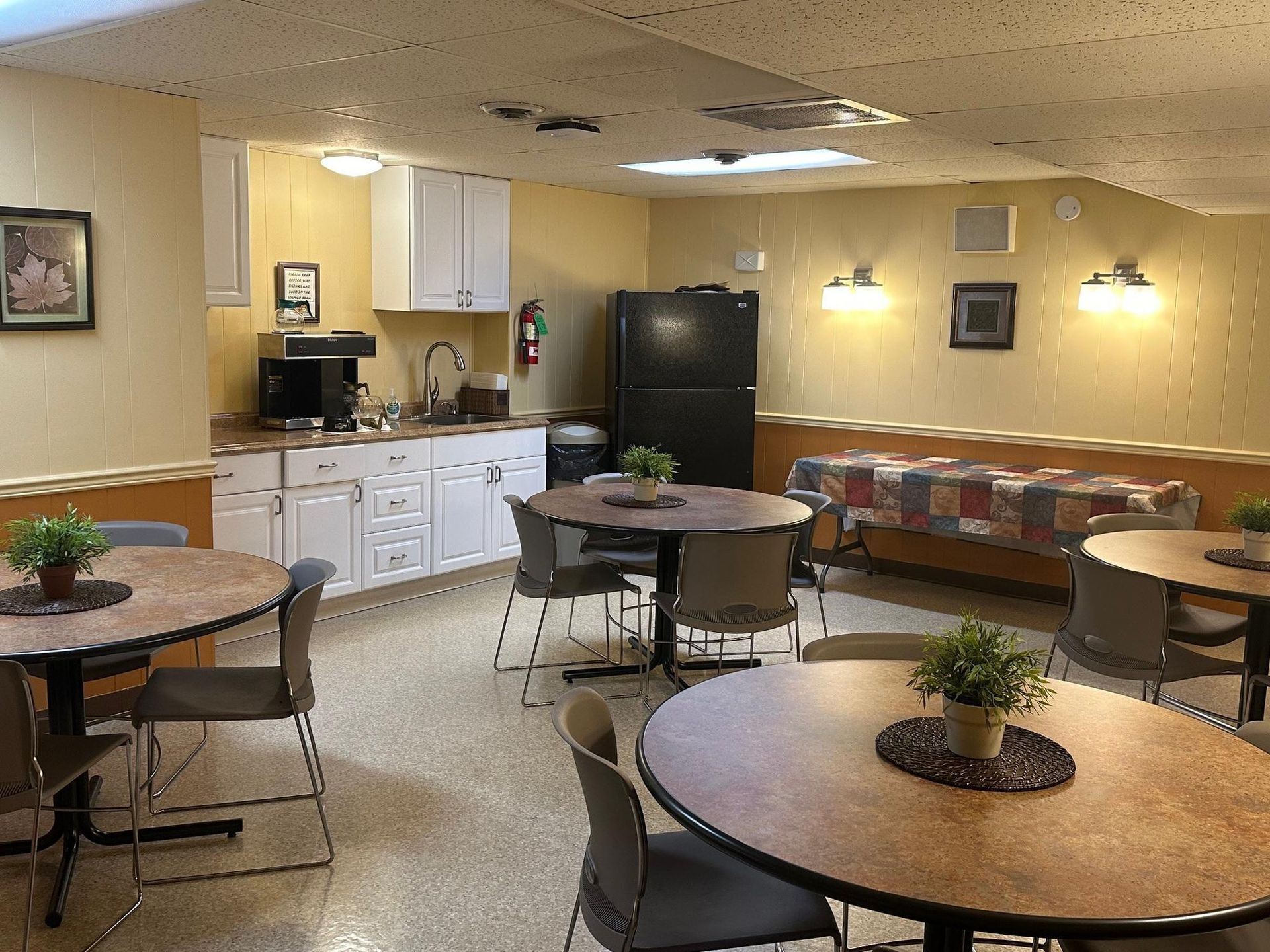 A small kitchen and dining area in a facility. Round tables with chairs and a buffet-style table.