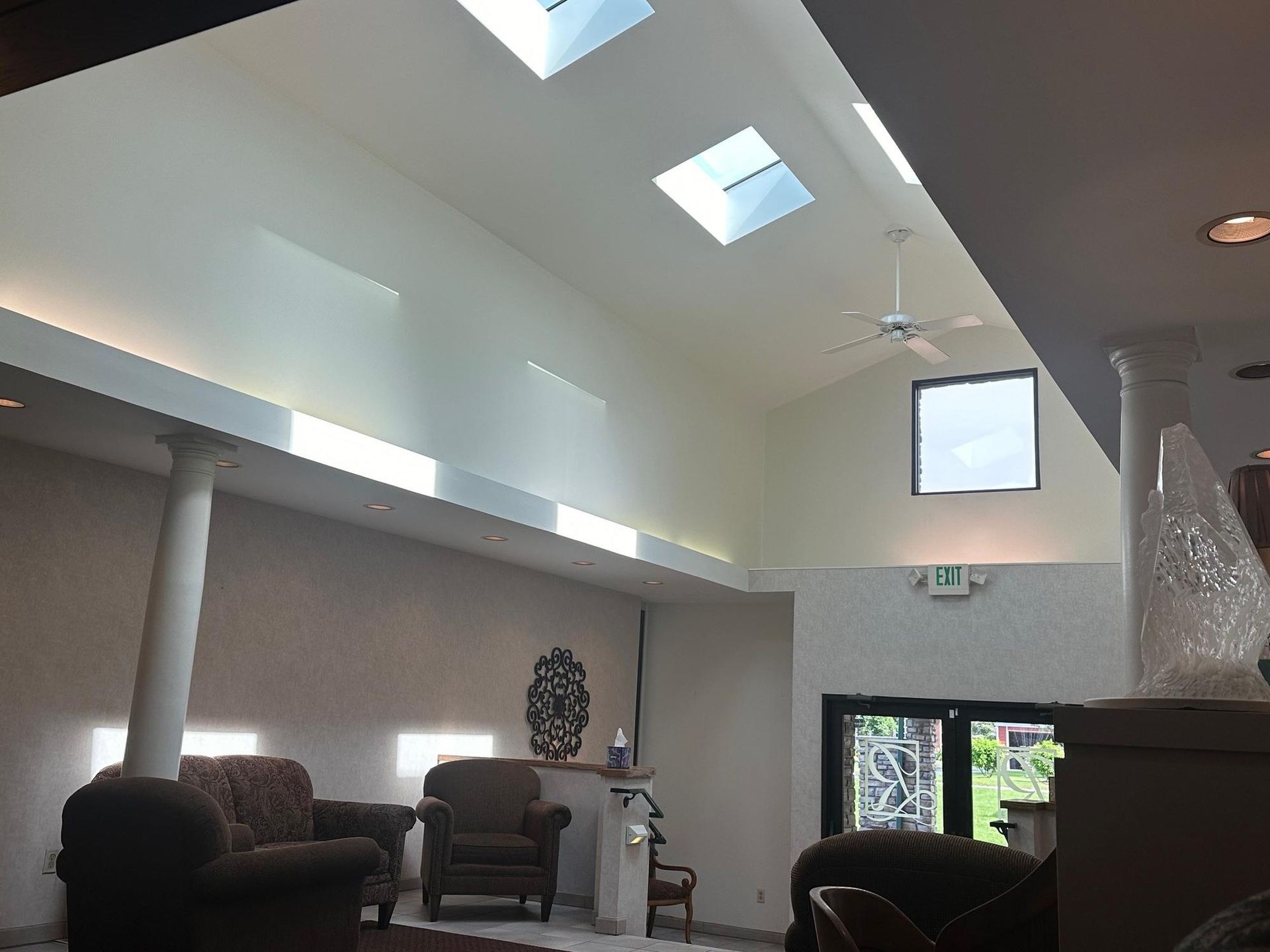 Bright interior with skylights, armchairs, columns, and a doorway.