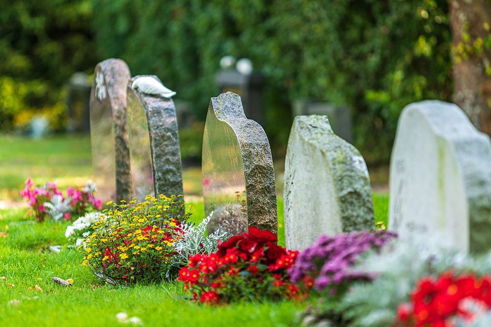 Headstones in a cemetery with colorful flowers and green grass.