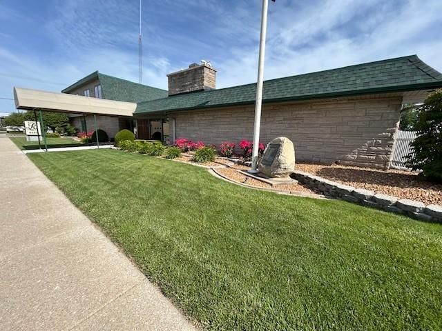 A building with a green roof, tan walls, and a well-manicured lawn with a flagpole.
