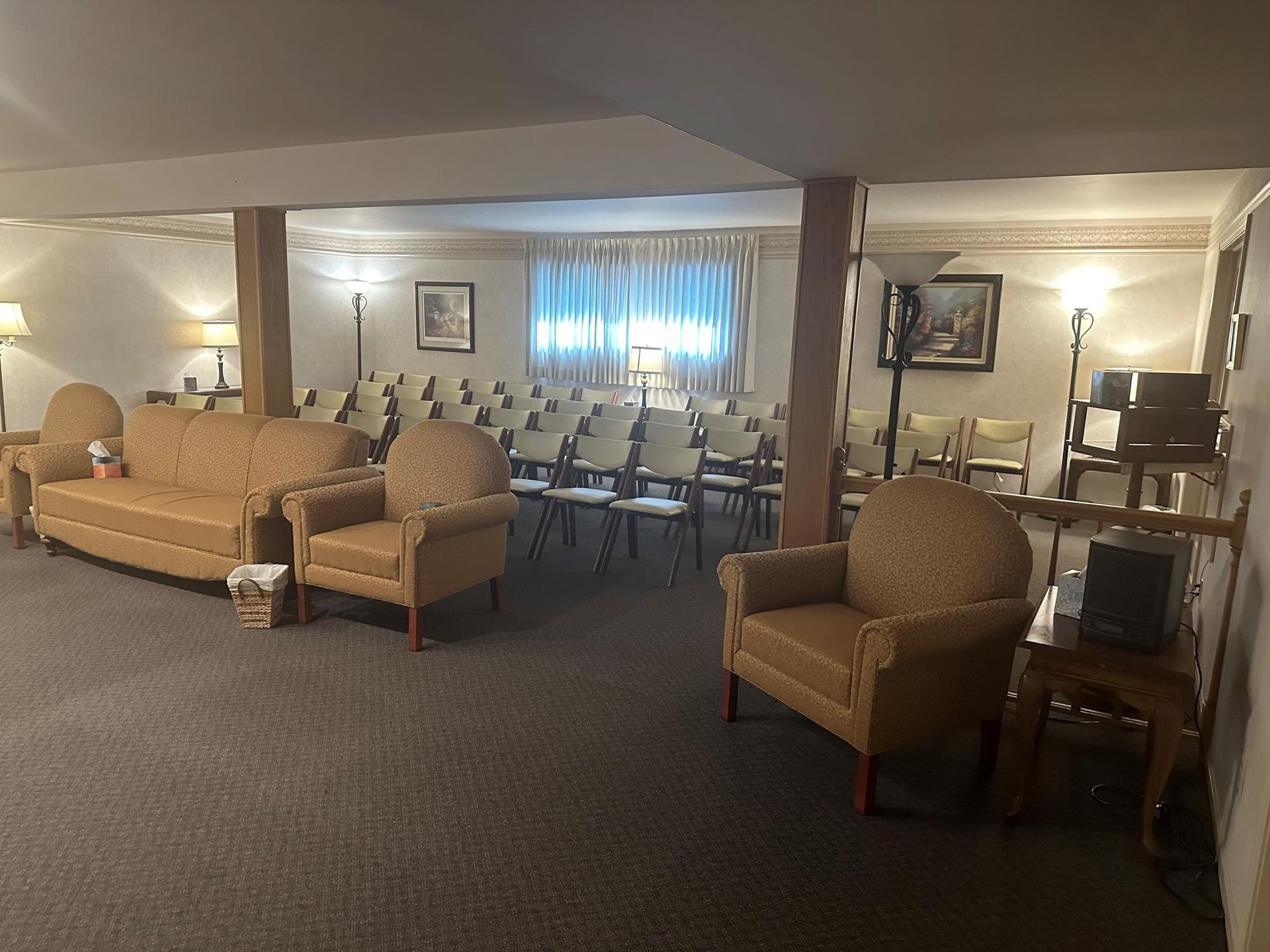 A room with chairs and couches, likely a reception area or event space. Dim lighting, neutral tones.