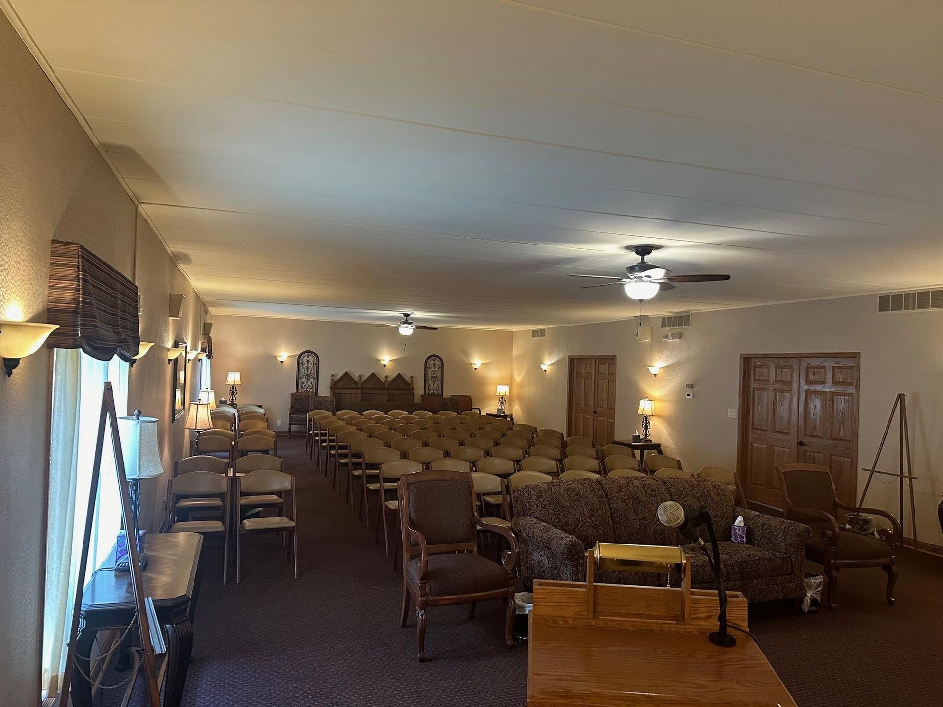 An empty chapel with rows of chairs, sconce lighting, and a podium.