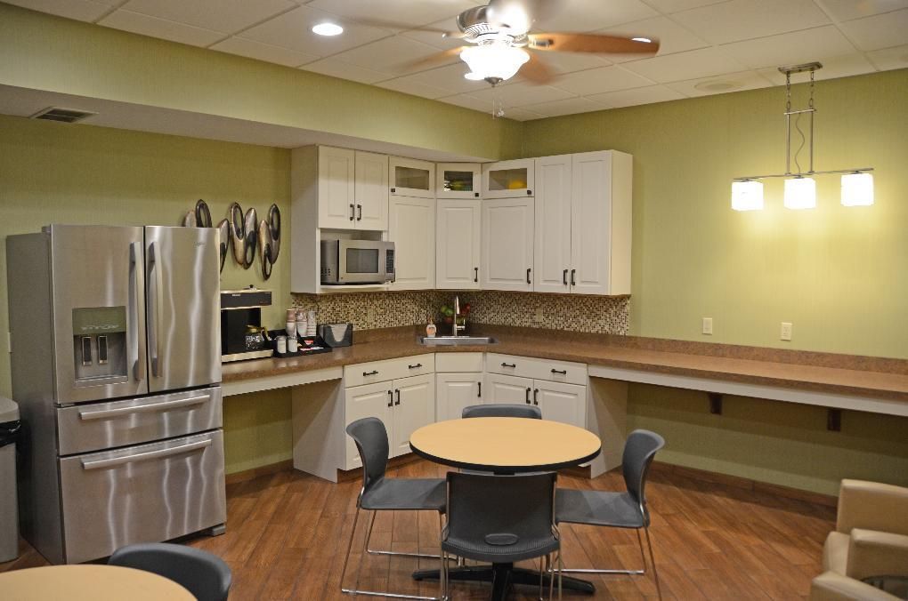 Kitchenette with white cabinets, stainless steel fridge, round table, and a ceiling fan.