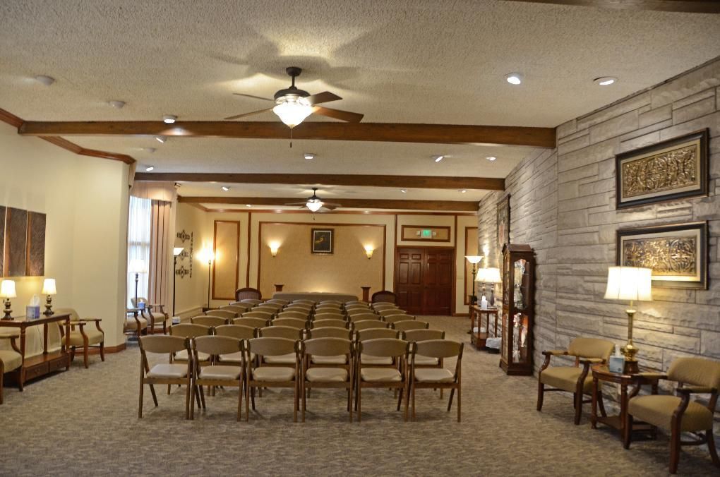 Interior of a funeral home chapel with rows of chairs, neutral walls, and wooden beams.