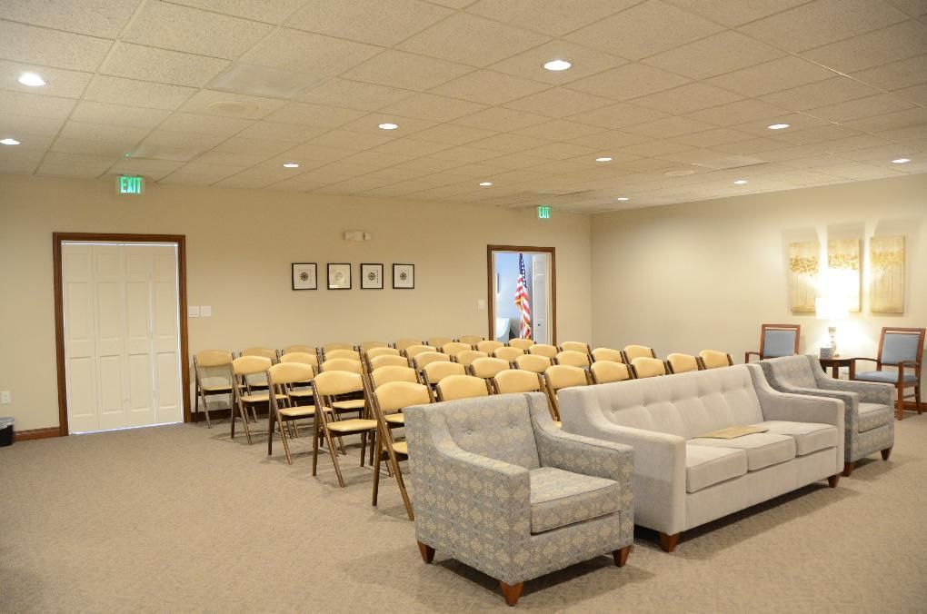 A meeting room with rows of chairs, sofas, and doors. The walls are beige, and the carpet is light brown.