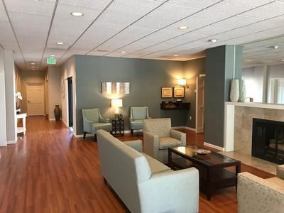 Waiting room with teal walls, fireplace, and seating. Wooden floors and recessed lighting.