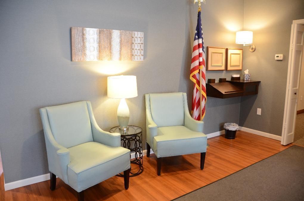 Two light blue armchairs in waiting room with American flag and desk.