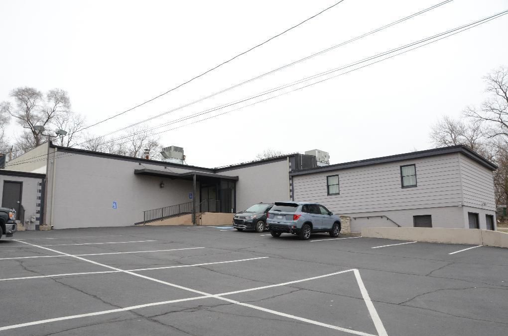 Building with parking lot. Gray exterior, ramp, parked cars, overcast sky.
