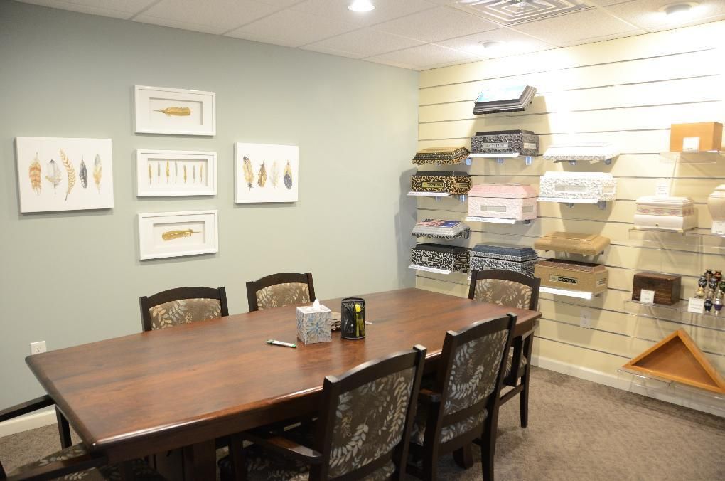 A conference room with a wooden table, chairs, and framed artwork. Display shelves hold various boxes.