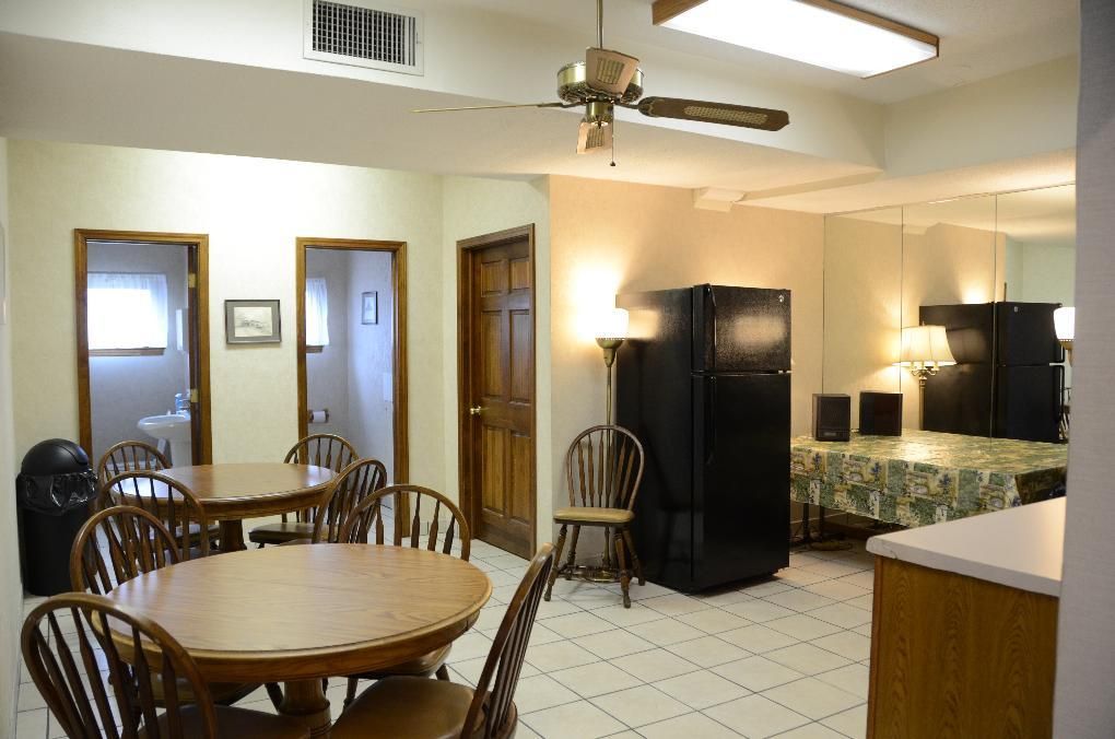 A dining area with round tables, chairs, and a black refrigerator. Doors and mirrors are visible.