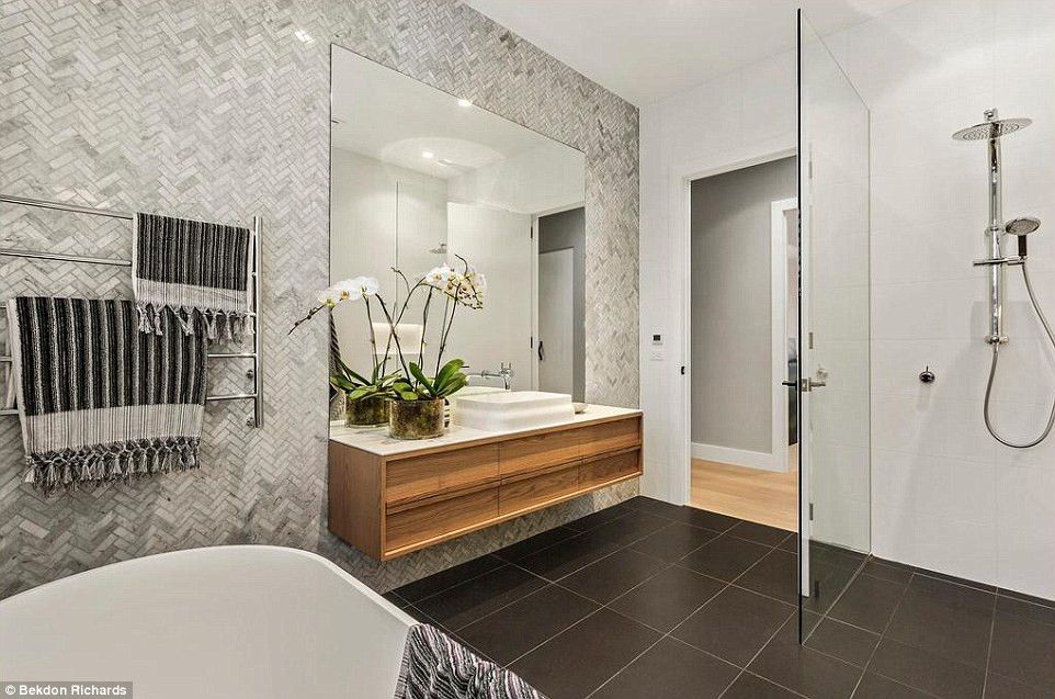 Modern bathroom with floating wooden vanity, patterned tile wall, black floor, and glass shower.